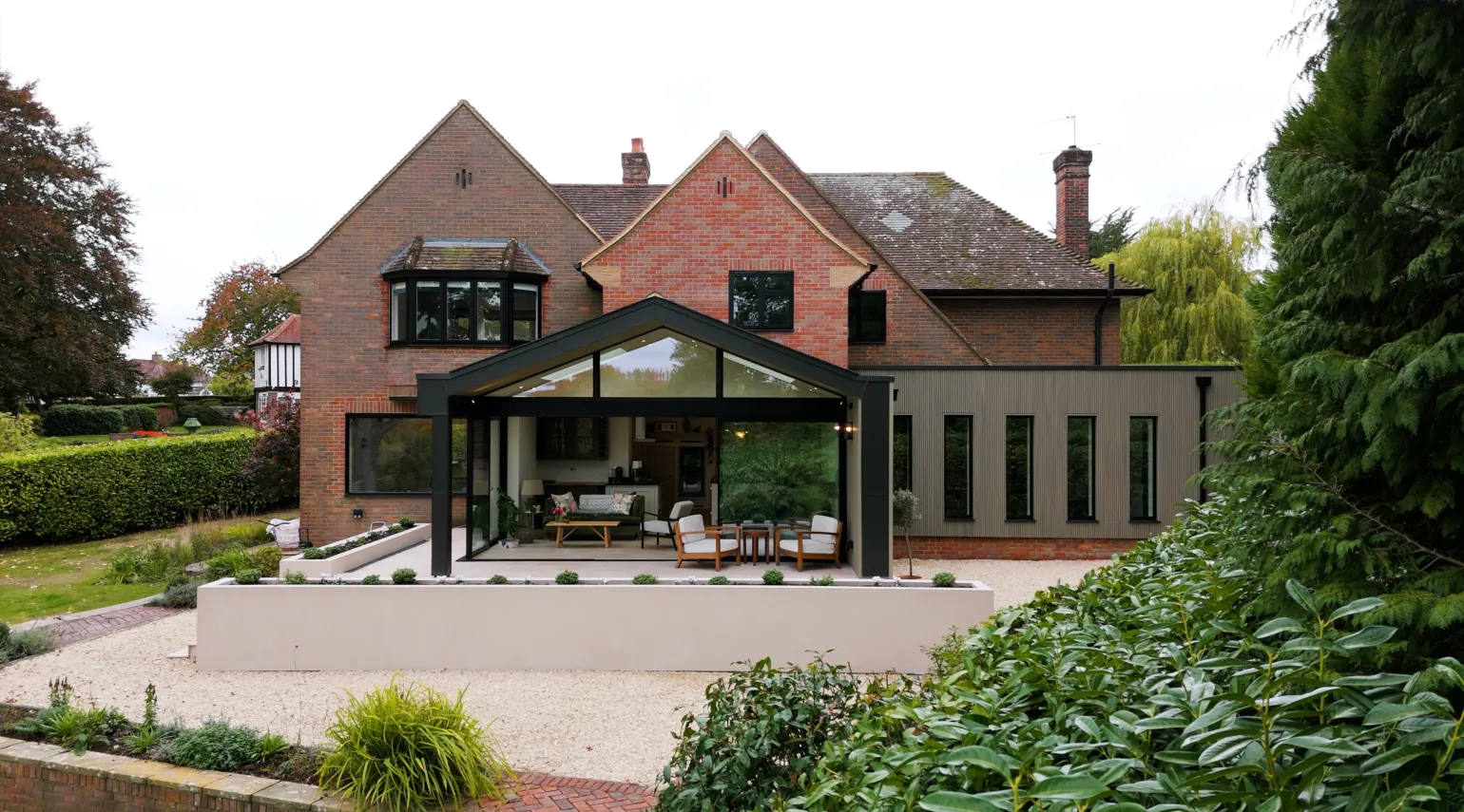 The cladding provides a light and natural-looking finish that works particularly well alongside the property's original red brickwork. The addition of cream paving reinforces the warm, neutral palette, while the black detailing used throughout the building provides a strong visual contrast.

Black frames, doors and windows create crisp definition against the lighter cladding, helping to emphasise the clean lines of the new extension and create a consistent contemporary aesthetic.

The slatted profile introduces texture and shadow lines across the new elevations, adding depth and visual interest.

The result is a balanced combination of traditional and contemporary materials, with the new cladding helping to visually tie together the different elements of the extension, orangery and entrance.

